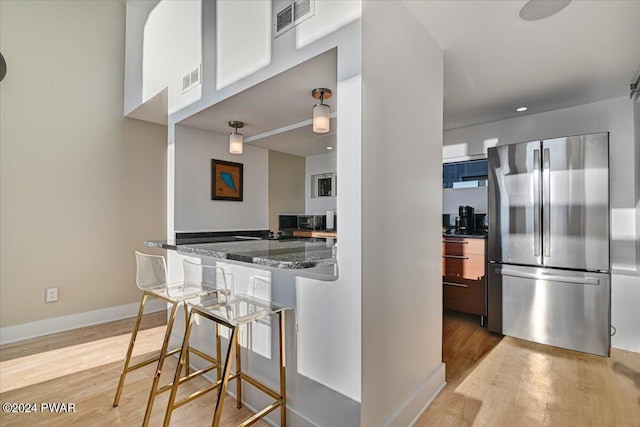 kitchen featuring dark stone counters, stainless steel refrigerator, and light hardwood / wood-style floors