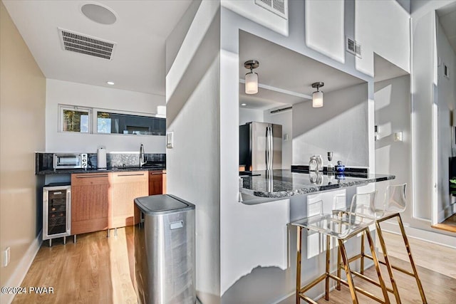 kitchen featuring dishwasher, a kitchen breakfast bar, wine cooler, light wood-type flooring, and stainless steel refrigerator