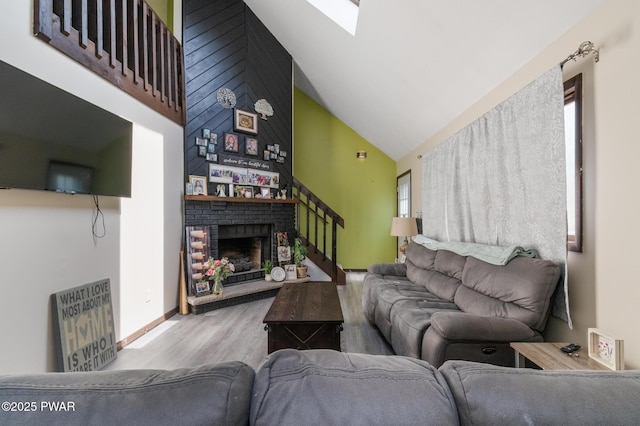 living area featuring a skylight, a brick fireplace, wood finished floors, stairway, and high vaulted ceiling
