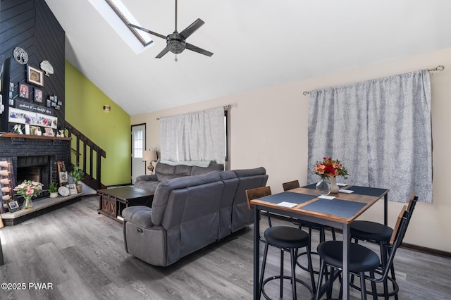 living room with high vaulted ceiling, a ceiling fan, wood finished floors, a skylight, and stairway