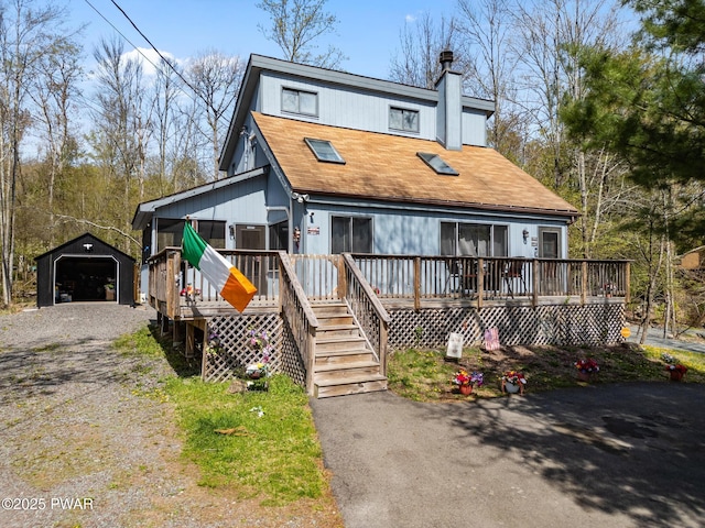 view of front facade featuring a detached garage, a deck, an outbuilding, a chimney, and gravel driveway