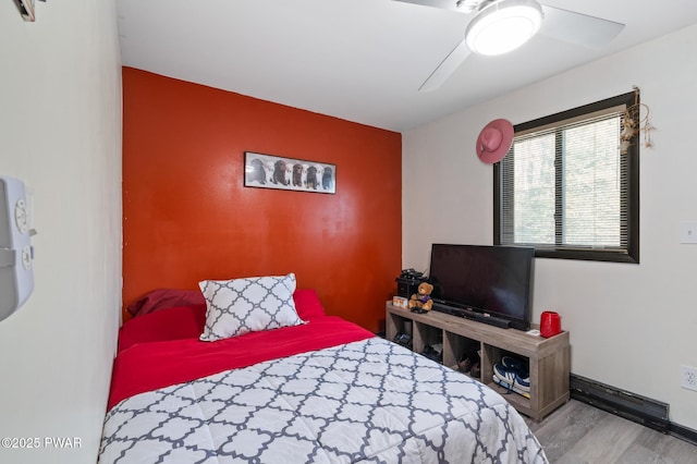bedroom with baseboards, a ceiling fan, an accent wall, and wood finished floors