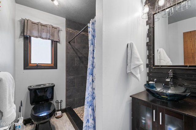 full bath with vanity, a textured ceiling, a tile shower, and toilet