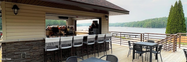 wooden terrace with outdoor dry bar, a water view, and a view of trees