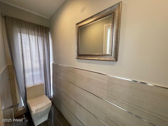 half bath with a wainscoted wall, toilet, tile walls, and a healthy amount of sunlight