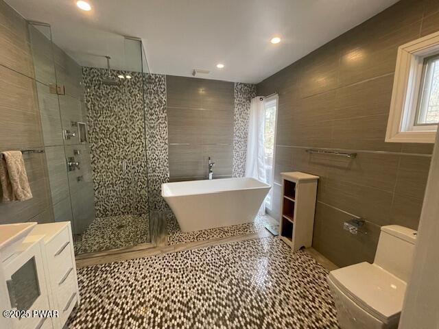 full bathroom featuring a shower stall, toilet, a freestanding tub, tile patterned floors, and tile walls