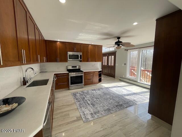 kitchen with a sink, light countertops, a baseboard heating unit, and stainless steel appliances