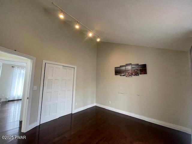 unfurnished bedroom featuring a closet, baseboards, dark wood-type flooring, and lofted ceiling