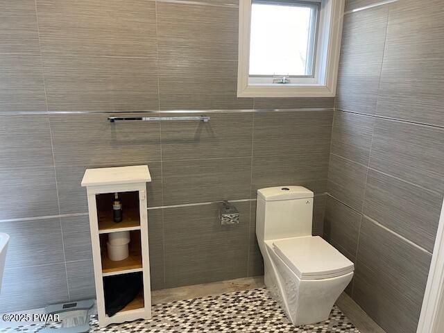 bathroom with tile patterned flooring, toilet, and tile walls