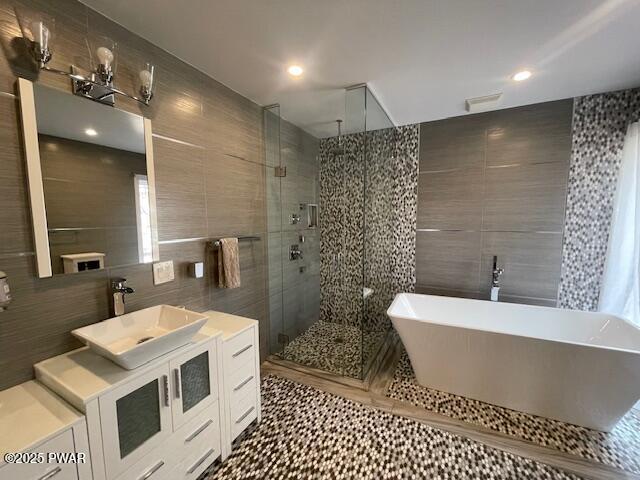 bathroom with tile patterned floors, a freestanding tub, tile walls, a shower stall, and vanity