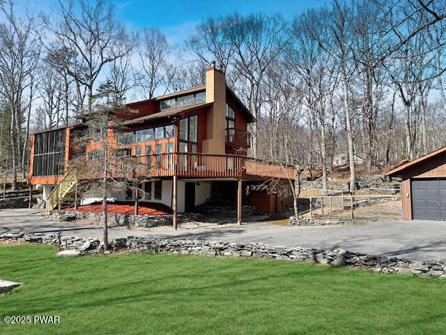 rear view of house featuring a wooden deck, stairs, a lawn, a chimney, and driveway