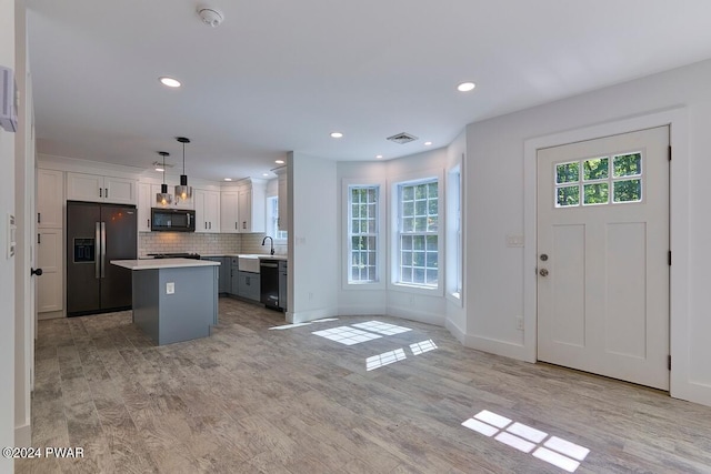 kitchen featuring white cabinetry, hanging light fixtures, a kitchen island, decorative backsplash, and black appliances