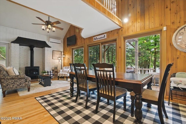 141 Arrowhead Cir, Newfoundland, PA 18445 - dining space featuring a wood stove, a wall mounted AC, wood walls, high vaulted ceiling, and a ceiling fan