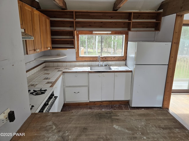 kitchen with exhaust hood, open shelves, a sink, tile counters, and white appliances