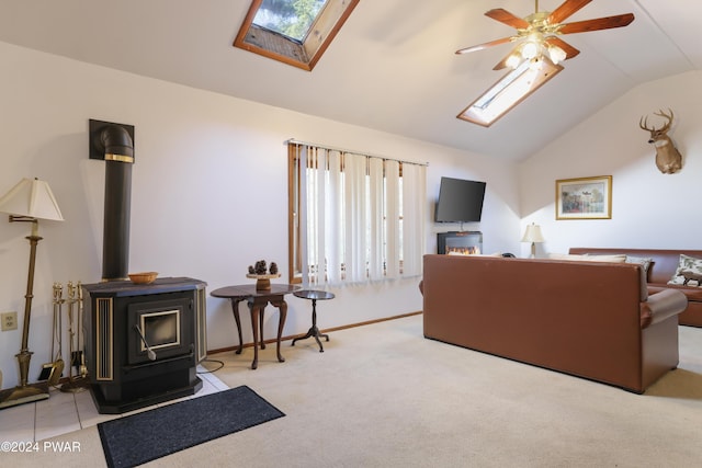 carpeted living room featuring a wood stove, ceiling fan, and vaulted ceiling with skylight