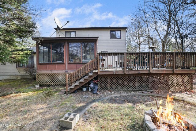 back of property featuring a wooden deck, a sunroom, and a fire pit