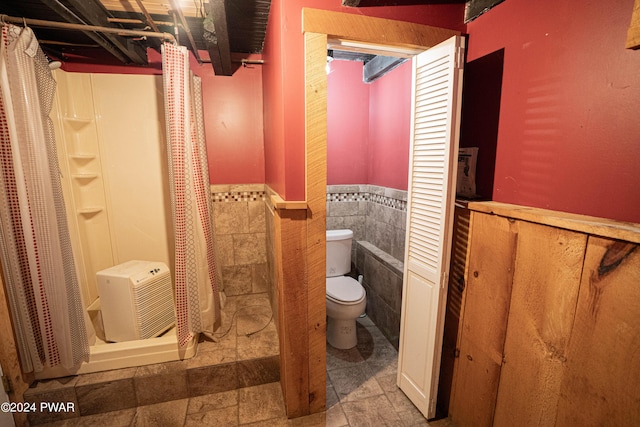 bathroom with a shower with shower curtain, toilet, and tile walls