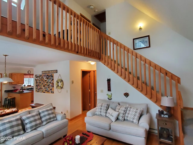 living room with a towering ceiling, light wood-type flooring, and baseboard heating