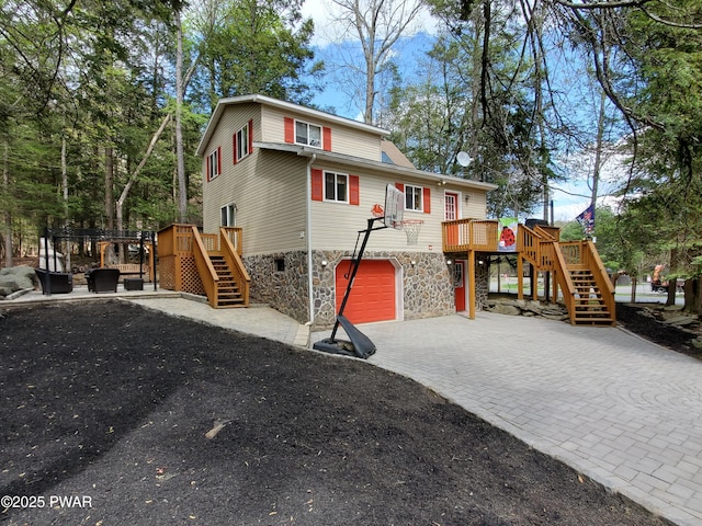 exterior space featuring a wooden deck, stone siding, decorative driveway, stairs, and an attached garage