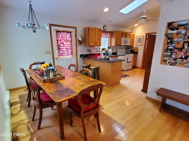 dining room with ceiling fan with notable chandelier, vaulted ceiling with skylight, and light wood-type flooring