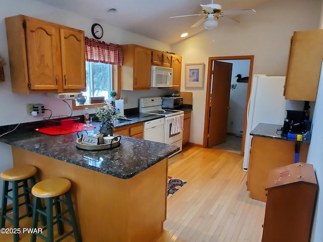 kitchen featuring lofted ceiling, a kitchen bar, kitchen peninsula, white appliances, and light hardwood / wood-style flooring