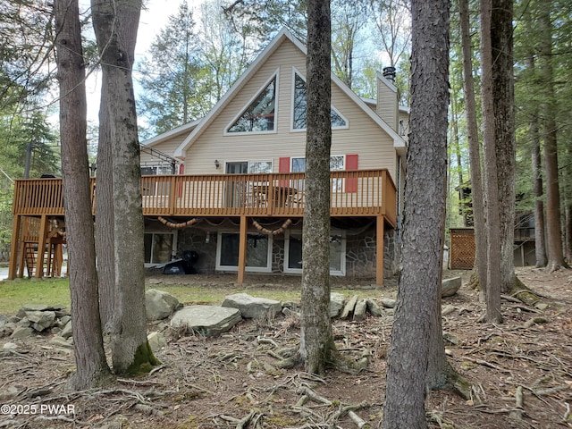 back of house with a wooden deck, a chimney, and stone siding