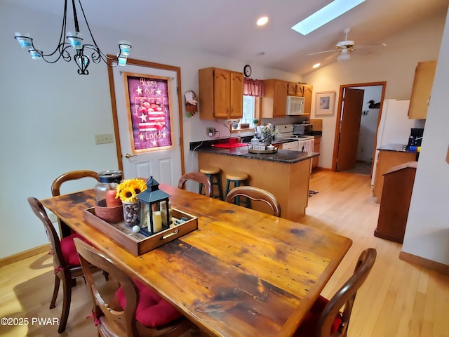 dining area with lofted ceiling with skylight, ceiling fan, and light wood-type flooring