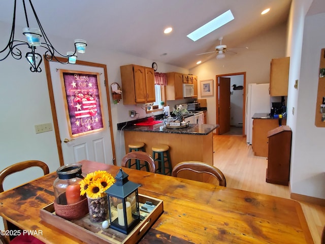 kitchen featuring white appliances, light hardwood / wood-style flooring, hanging light fixtures, lofted ceiling with skylight, and kitchen peninsula