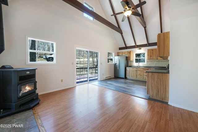 kitchen featuring high vaulted ceiling, stainless steel refrigerator with ice dispenser, a sink, dark countertops, and a wood stove