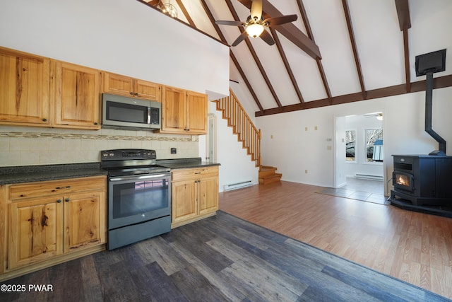 kitchen featuring backsplash, dark countertops, appliances with stainless steel finishes, baseboard heating, and a wood stove