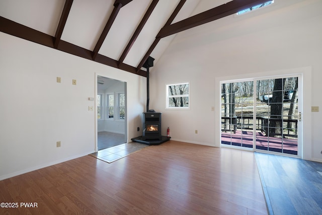 unfurnished living room featuring wood finished floors, baseboards, high vaulted ceiling, a wood stove, and beamed ceiling