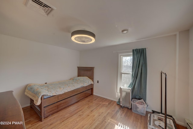 bedroom with light hardwood / wood-style floors, radiator heating unit, and a baseboard radiator