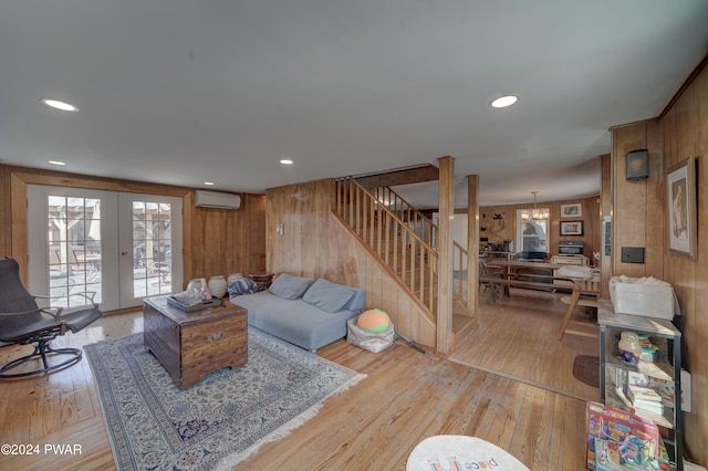 living room with a wall mounted air conditioner, light hardwood / wood-style floors, wooden walls, and french doors