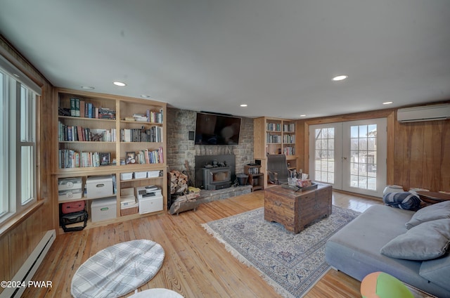 living room with a wood stove, wooden walls, a baseboard radiator, light hardwood / wood-style floors, and a wall unit AC