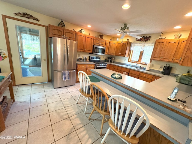 kitchen with stainless steel appliances, a peninsula, a ceiling fan, light countertops, and brown cabinets