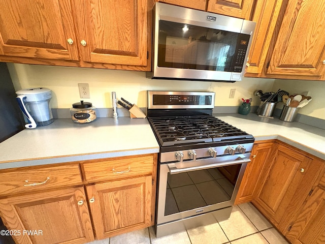 kitchen featuring appliances with stainless steel finishes, light countertops, light tile patterned floors, and brown cabinetry