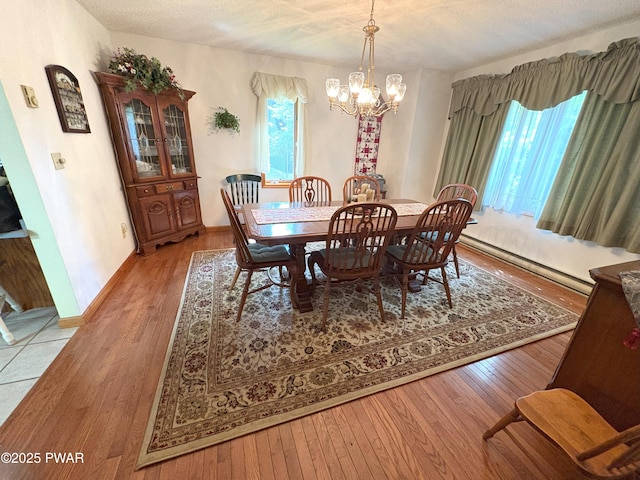 dining room with a chandelier, wood-type flooring, baseboard heating, a textured ceiling, and baseboards