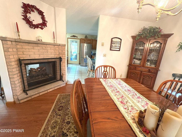 dining space featuring wood finished floors, a textured ceiling, and a brick fireplace