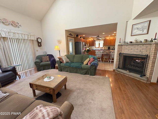living area featuring high vaulted ceiling, light wood-style floors, a fireplace, and ceiling fan
