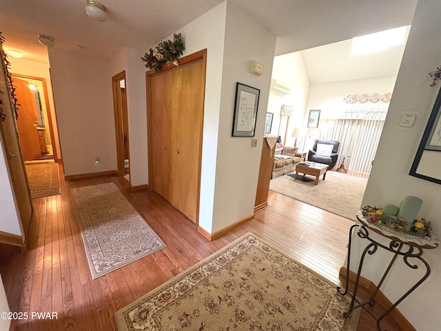 hall featuring hardwood / wood-style flooring, baseboards, and vaulted ceiling