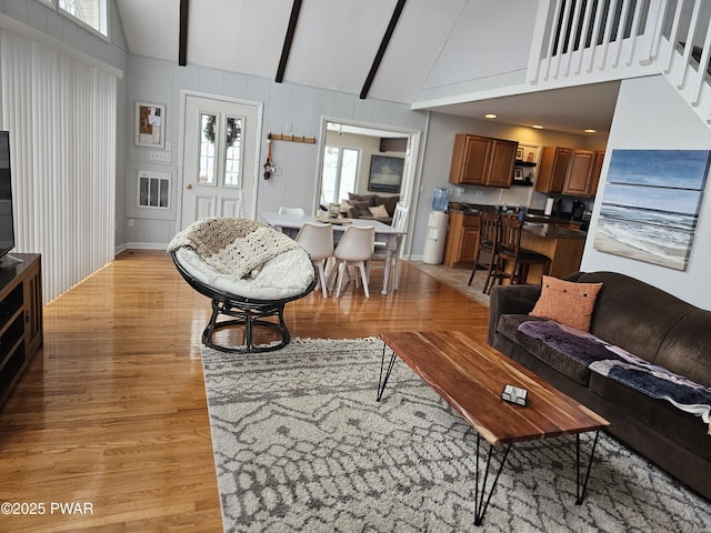 living room with beamed ceiling, light hardwood / wood-style floors, and high vaulted ceiling