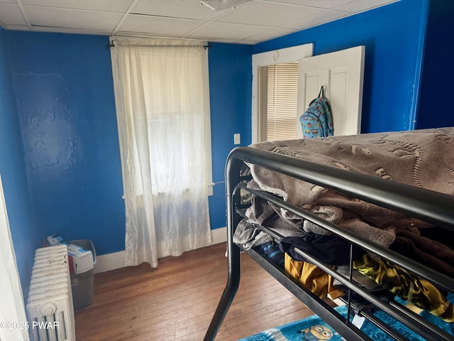 bedroom with radiator heating unit, wood-type flooring, and a paneled ceiling