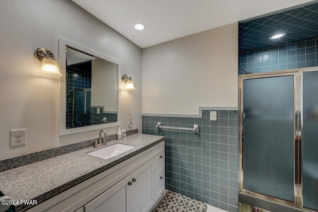 bathroom featuring tile patterned floors, vanity, a shower with shower door, and tile walls