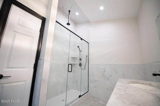 bathroom featuring a sink, recessed lighting, a marble finish shower, tile walls, and wainscoting