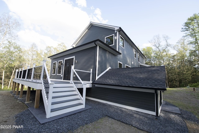 exterior space with stairway, a deck, and a shingled roof