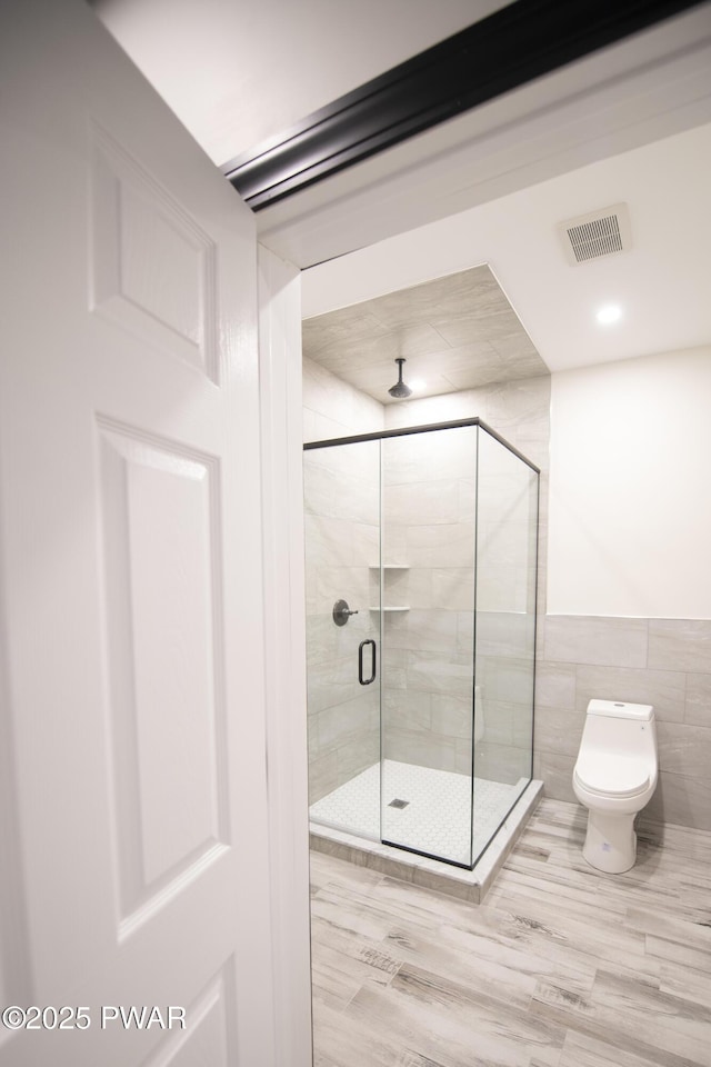 full bath with a shower stall, toilet, tile walls, and visible vents