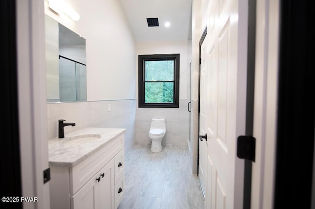 bathroom featuring vanity, visible vents, a shower stall, tile walls, and toilet