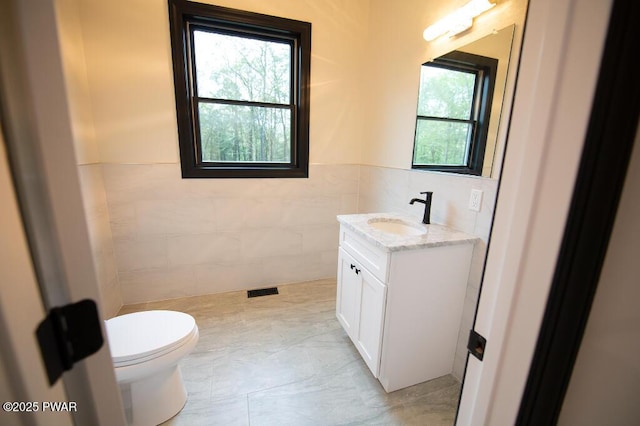 bathroom featuring visible vents, toilet, tile walls, and vanity