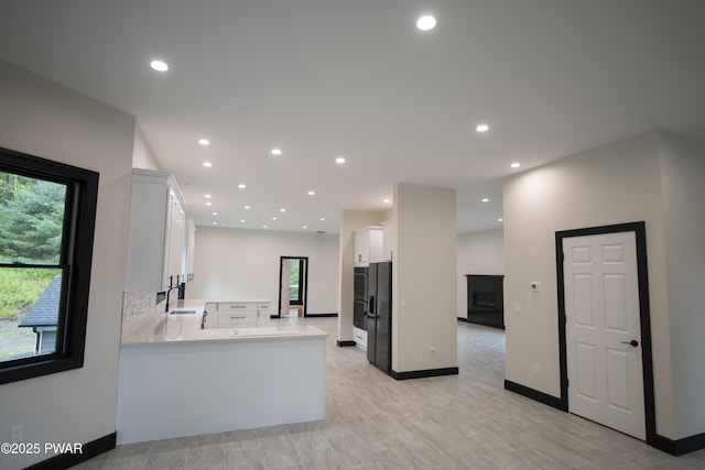 kitchen with light countertops, recessed lighting, a peninsula, white cabinets, and a sink