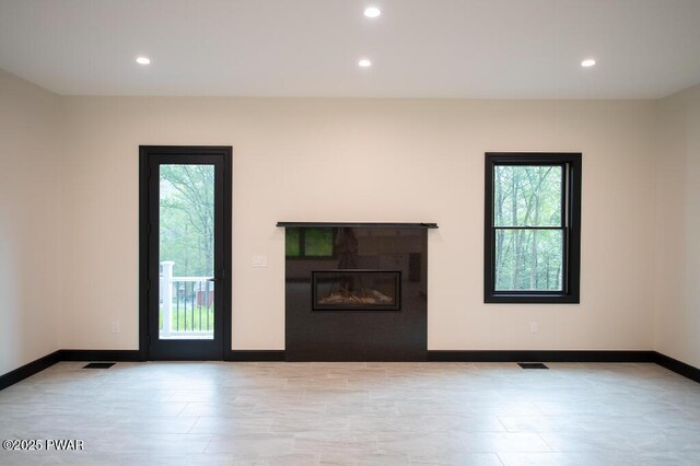 unfurnished living room featuring recessed lighting, visible vents, plenty of natural light, and a glass covered fireplace